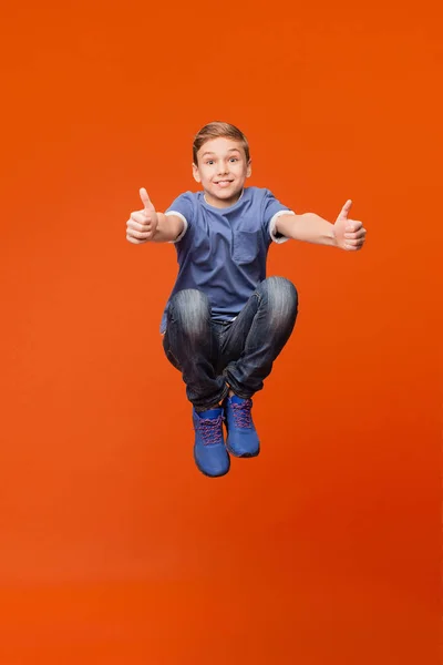 Skola pojke hoppar och gör tummen upp — Stockfoto