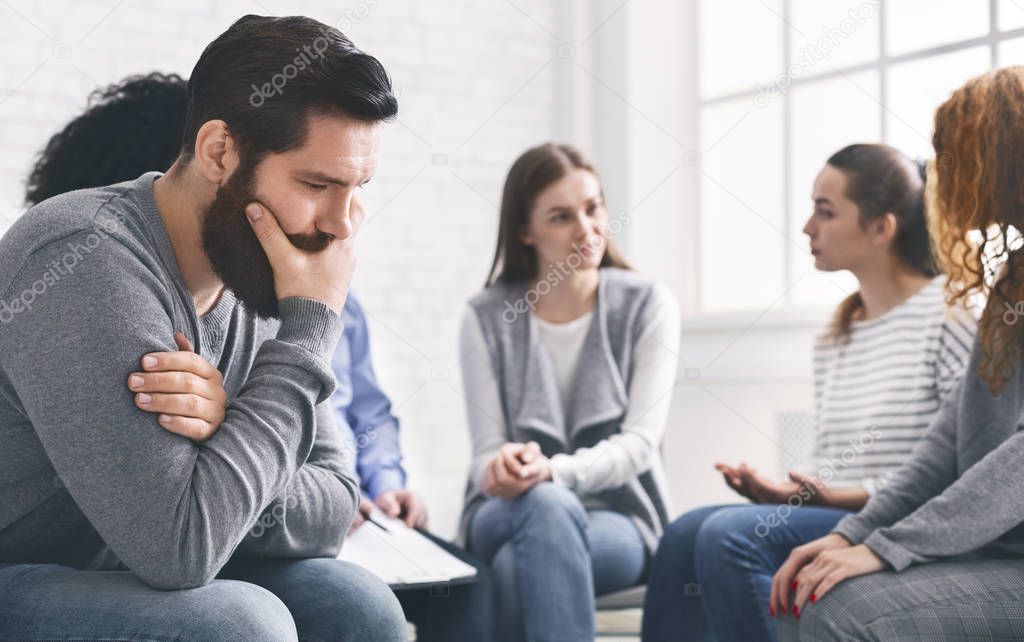 Depressed man sitting at rehab group therapy