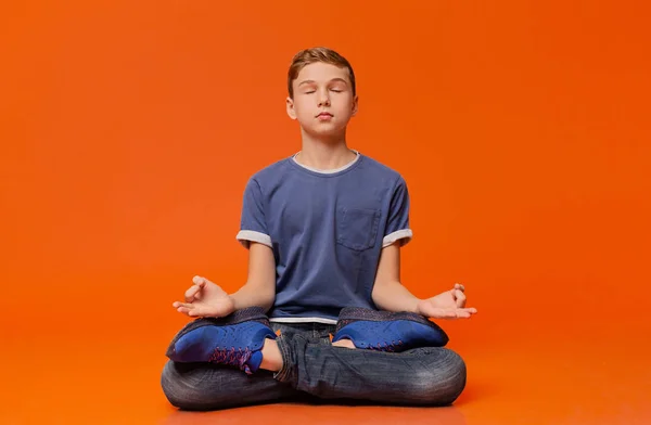 Niño tranquilo sentado en el suelo y meditando en posición de loto . — Foto de Stock