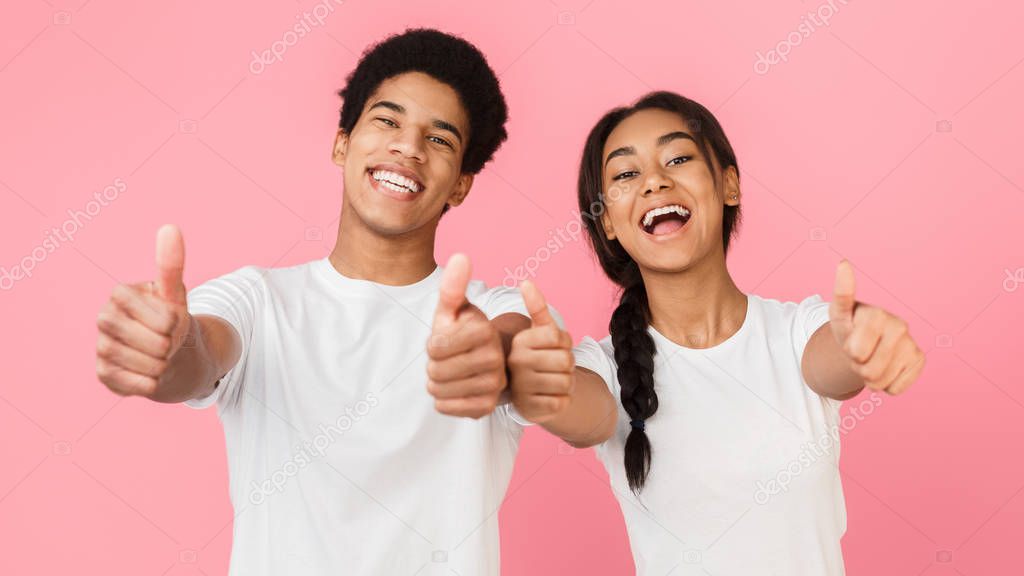 Happy teenage couple showing thumbs up over pink background