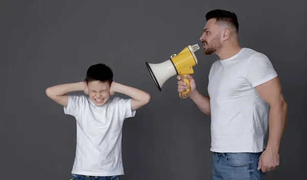 Отец с мегафоном, кричащий на сына, закрывающего уши — стоковое фото