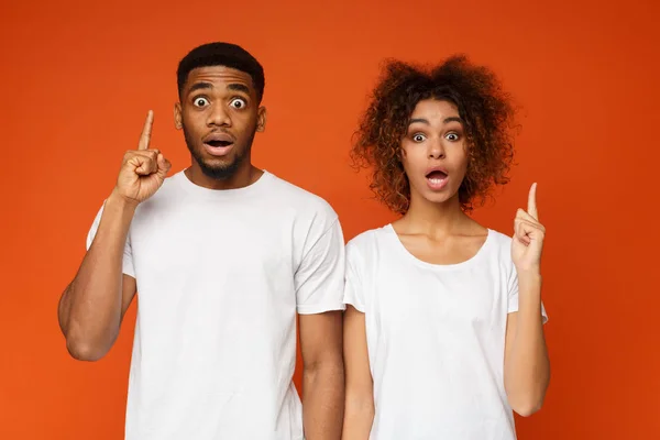 Stunned black man and woman pointing upward with opened mouths — Stock Photo, Image