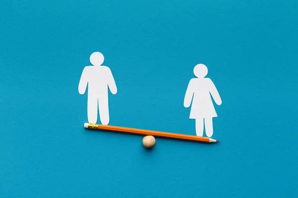 Female figure outweigh male on seesaw, blue background — Stock Photo, Image