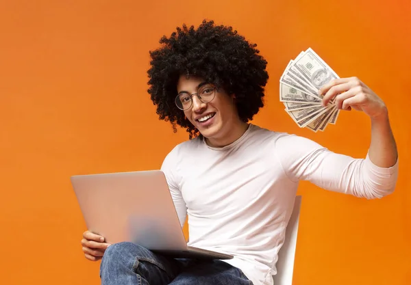 Šťastný chlap pracuje na notebooku a ukazuje spoustu peněz — Stock fotografie