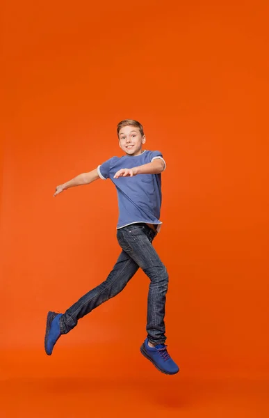 Netter Junge tanzt, springt in der Luft auf orangefarbenem Hintergrund — Stockfoto