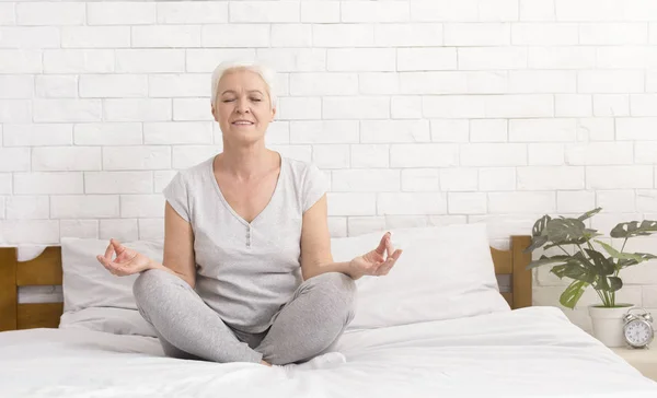 Mulher sênior meditando na posição de lótus na cama — Fotografia de Stock