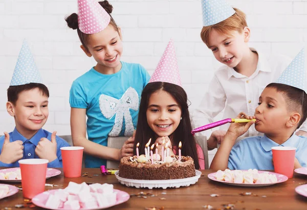 Birthday party. Girl making wish, looking at cake at home