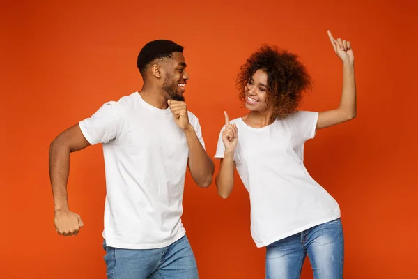 Positive black guy and girl dancing on orange background — Stock Photo, Image