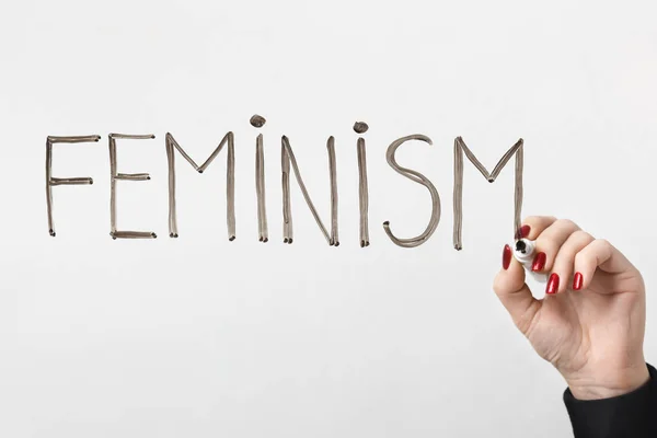 Female hand writing word FEMINISM on glass board — Stock Photo, Image