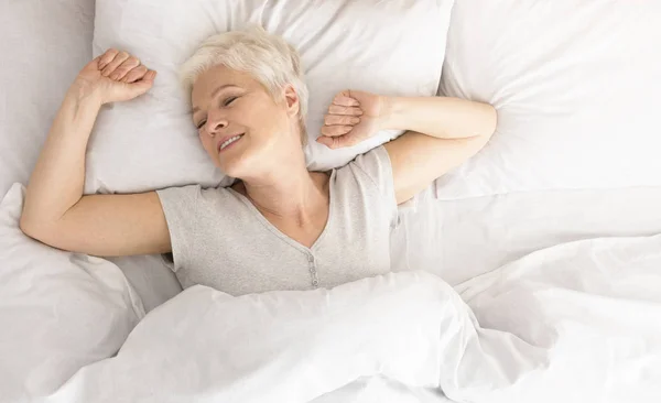 Senior woman lying down in her bed at home — Stock Photo, Image