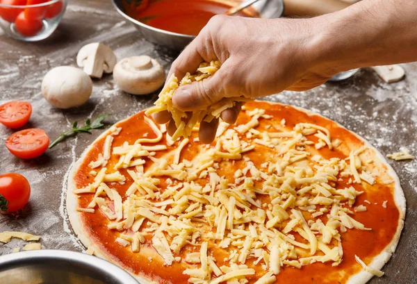 Mann, der die Pizza zubereitet, fügt Käse auf Pizzaboden hinzu — Stockfoto