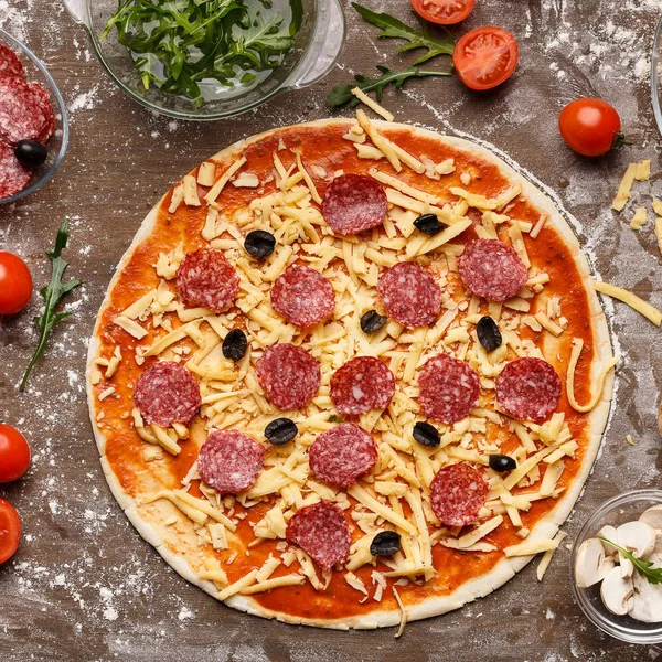 Ungebackene Pizza mit Käse, Salami und Oliven, von oben — Stockfoto