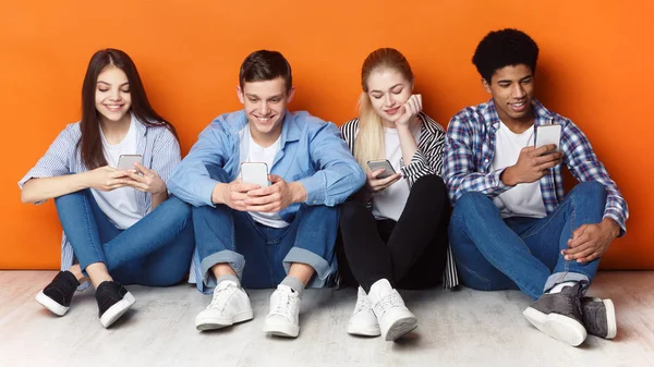 Adicción a Internet. Adolescentes con teléfonos inteligentes, pared naranja —  Fotos de Stock