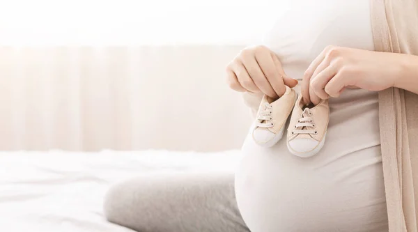 Small shoes for unborn baby on belly of pregnant woman — Stock Photo, Image