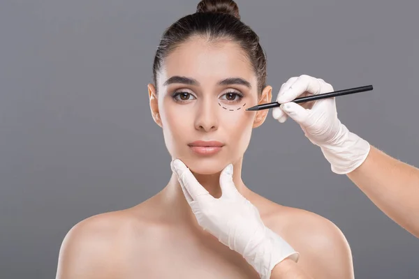 Doctor drawing marks on female face before procedure — Stock Photo, Image