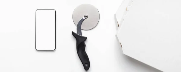 Phone with blank screen, pizza cutter and cardboard box — Stock Photo, Image