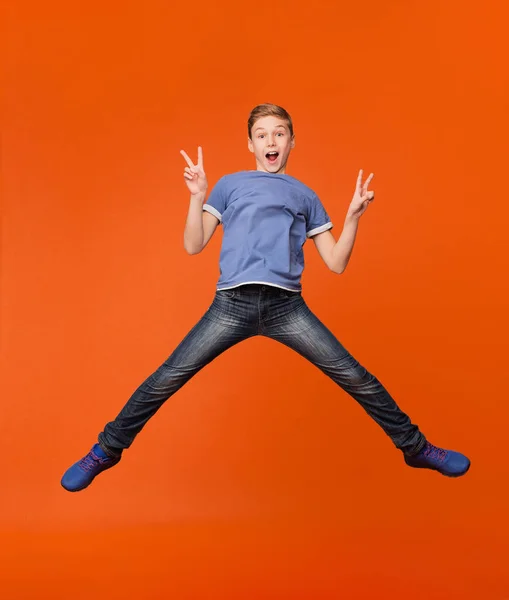 Boy jumping and showing peace gesture on orange — Stock Photo, Image