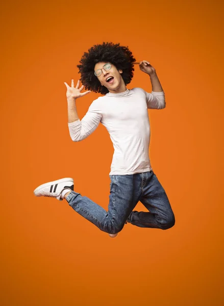 Ecstatic and amazed black guy jumping on orange background