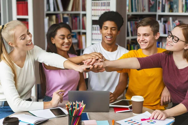 Group of students putting their hands up together in library — Stock Photo, Image