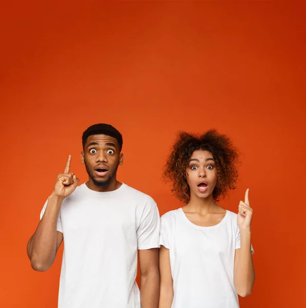 Afroamericano conmocionado hombre y mujer apuntando con los dedos hacia arriba —  Fotos de Stock