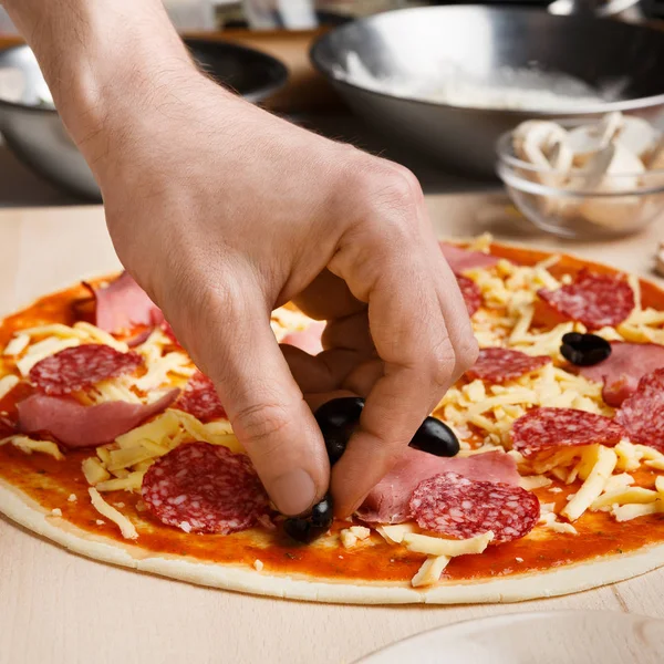 Pizza-Kunst. Mann vermischt Pizza mit Oliven — Stockfoto