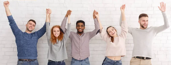 Conceito de unidade. Amigos com as mãos para cima sobre parede de tijolo branco — Fotografia de Stock