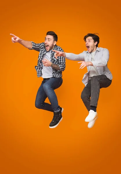Двоє схвильованих чоловіків спрямовують пальці геть, стрибаючи над тлом — стокове фото