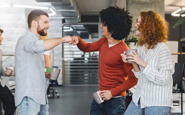 Happy male colleagues giving fist bump during coffee break