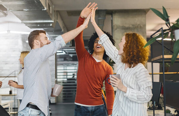 Happy coworkers having fun, giving high five during coffee break