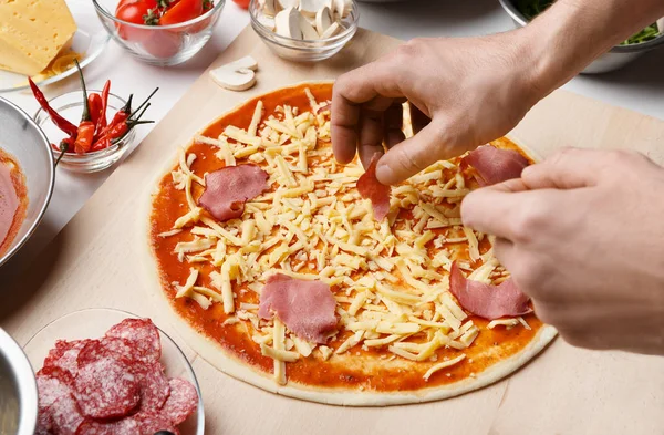 Mann fügt Schinken auf Pizzaboden mit Käse hinzu — Stockfoto