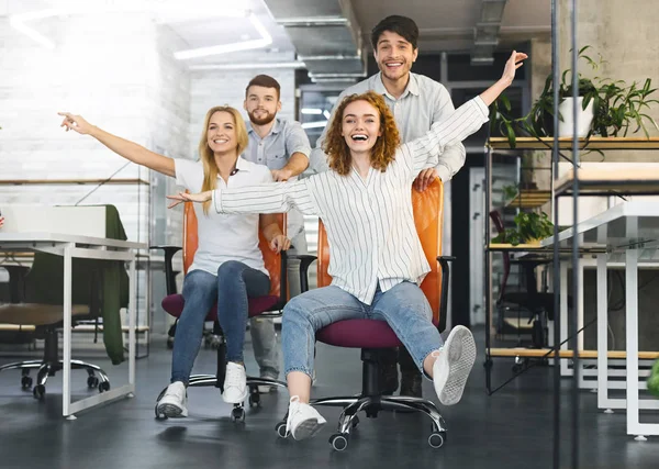 Happy colleagues having fun at workplace, making office chair race