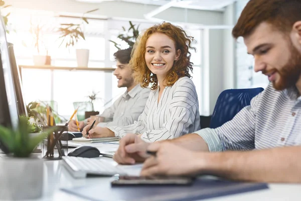 Fröhliches rothaariges Mädchen lächelt in die Kamera, arbeitet beim Coworking — Stockfoto