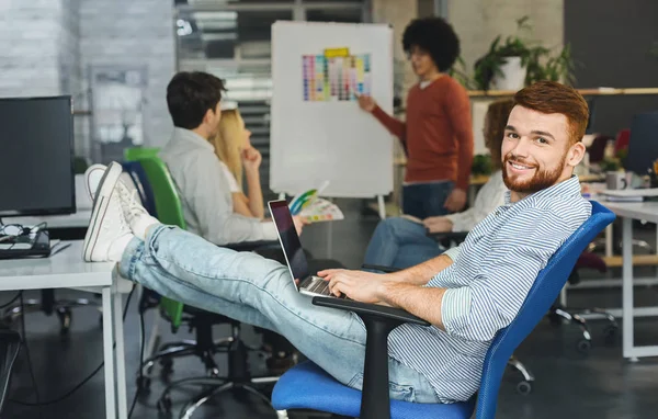 Cheerful millennial man working on laptop in coworking