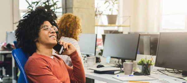 Cheerful african-american guy talking on phone at workplace