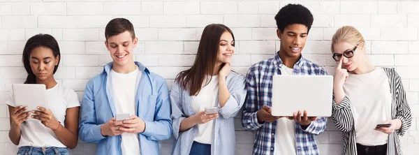 Students with various gadgets and laptop against white wall — Stock Photo, Image