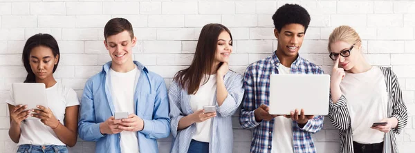 Étudiants avec divers gadgets et ordinateur portable contre le mur blanc — Photo