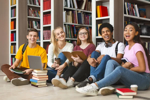 Grupa różnych nastoletnich kolegów siedzących na podłodze biblioteki — Zdjęcie stockowe