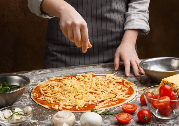 Pizza zubereiten. Frau würzt Pizza mit Käse — Stockfoto