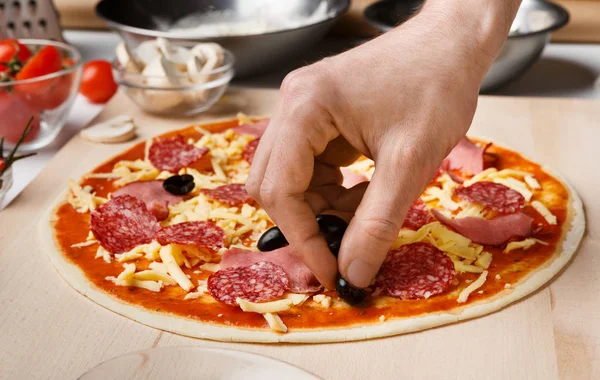 Pizzaiolo fügt schwarze Oliven zur Pizza hinzu und dekoriert sie — Stockfoto