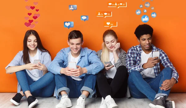 Adolescentes con teléfonos inteligentes charlando en las redes sociales, pared naranja —  Fotos de Stock