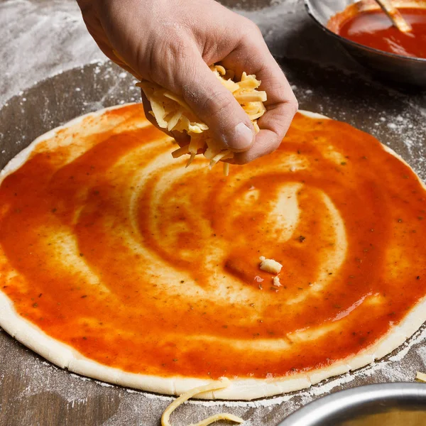 Προετοιμάζω ιταλικό πιάτο. Ο άνθρωπος προσθέτει τυρί στη βάση της πίτσας — Φωτογραφία Αρχείου