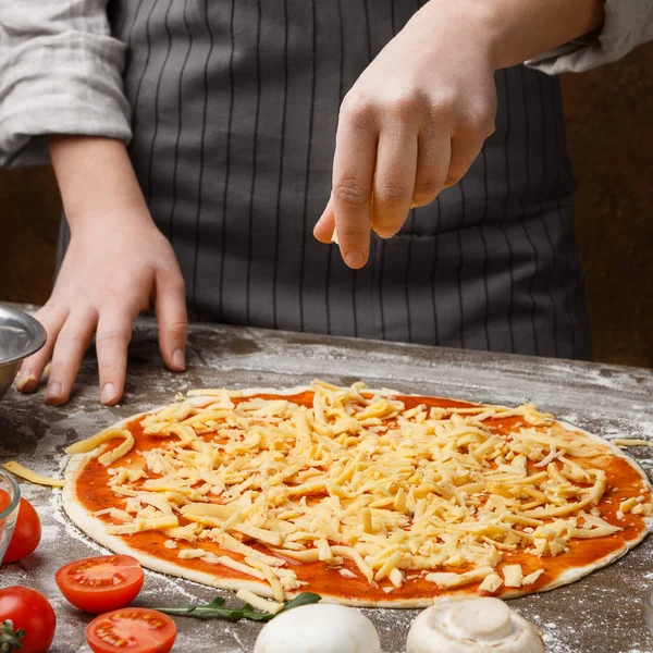 Koch bestreut Pizza mit Käse in Küche — Stockfoto