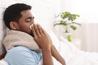 Young sick man in bed cleaning snotty nose