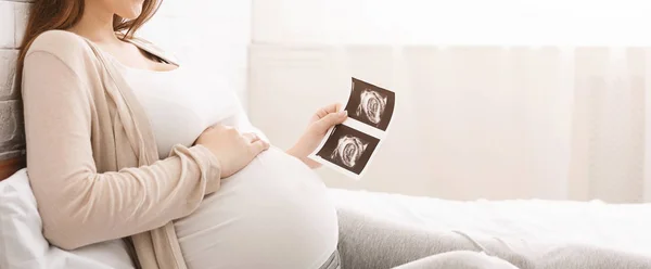 Mujer embarazada sosteniendo imagen de ultrasonido acostada en la cama —  Fotos de Stock