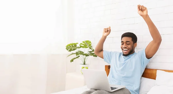 Young happy black guy celebrating success in bed