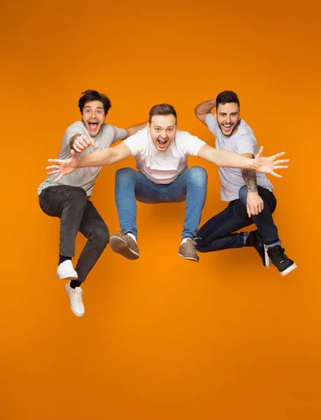 Возбужденные друзья прыгают вместе через оранжевый фон — стоковое фото