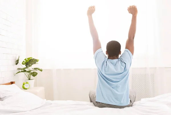 Fiatal férfi ébredt fel az ágyban, és nyújtás a karját — Stock Fotó