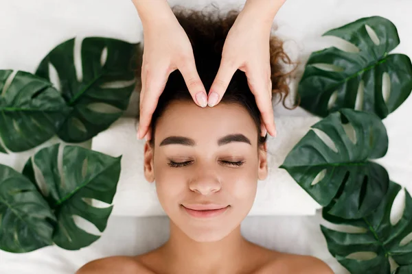 Menina afro-americana recebendo massagem facial com folhas tropicais ao redor — Fotografia de Stock