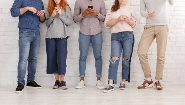 Young people texting on their smartphones, leaning on wall