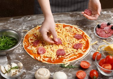 Kadın ev yapımı pepperoni pizza hazırlıyor, salam ekliyor.